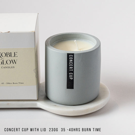 Gray candle in a container with a box labeled 'Noble Glow Candles' on a white surface.