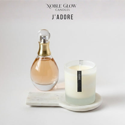 Perfume bottle and candle on a marble tray with 'Noble Glow Candles J'Adore' branding.