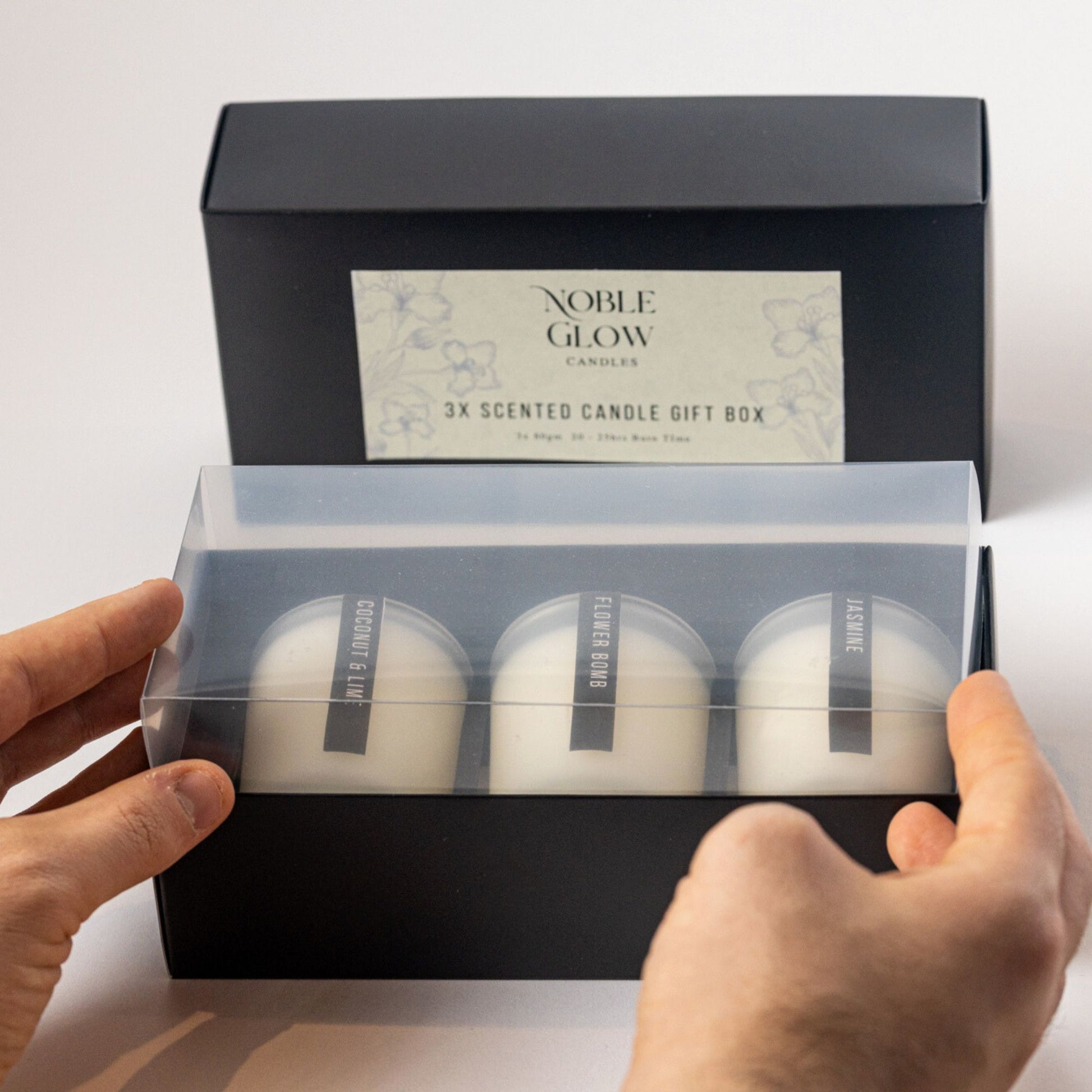 Noble Glow scented candles in a gift box held by hands against a light background