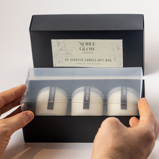 Noble Glow scented candles in a gift box held by hands against a light background