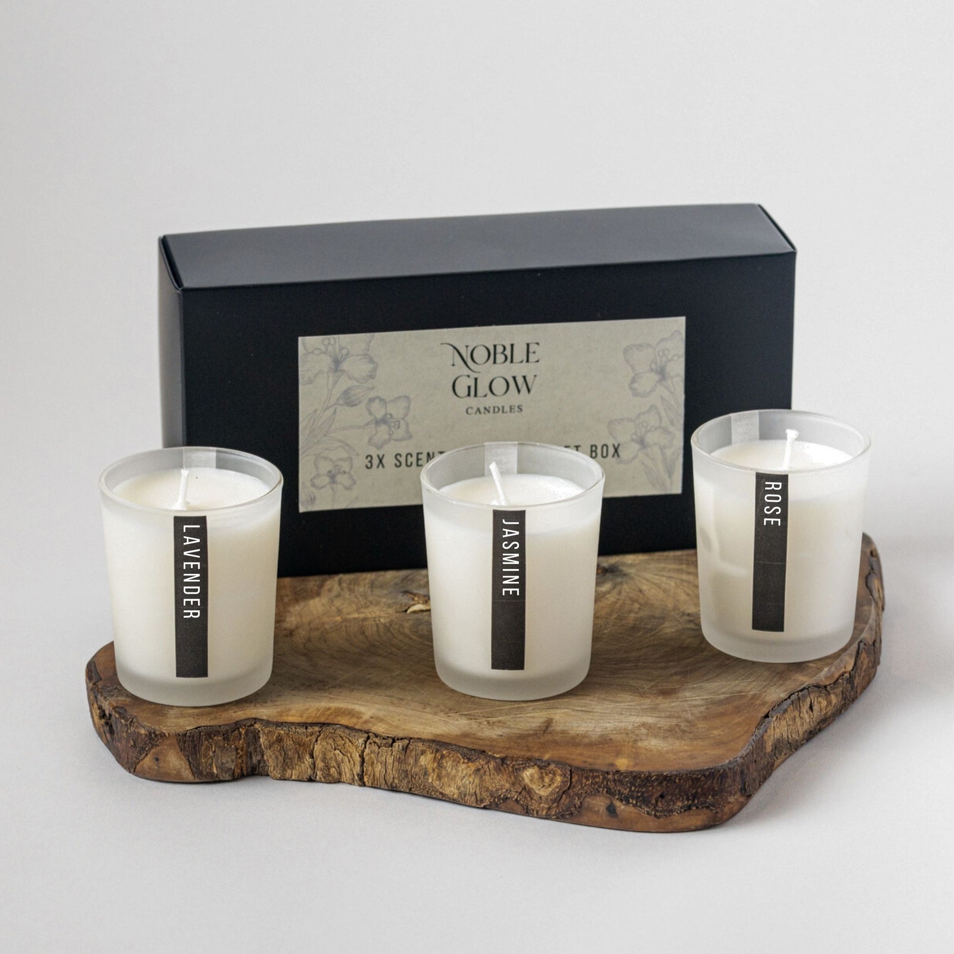Three scented candles on a wooden tray with a 'Noble Glow' box in the background.