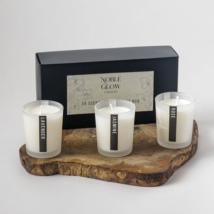 Three scented candles on a wooden tray with a 'Noble Glow' box in the background.
