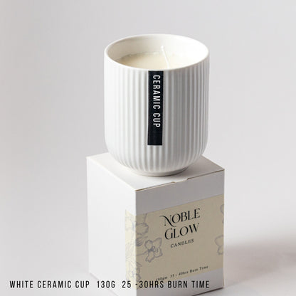 White ceramic cup on a box with 'Noble Glow Candles' branding on a gray background