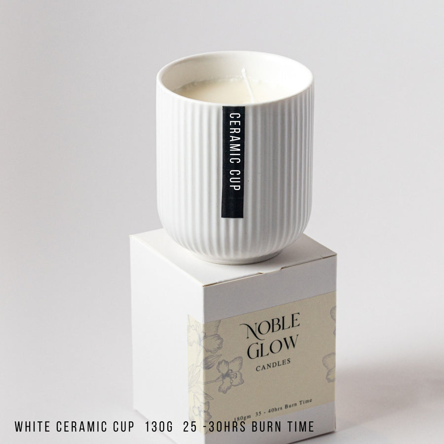 White ceramic cup on a box with 'Noble Glow Candles' branding on a gray background